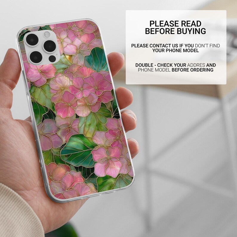 May include: A clear phone case featuring a floral design with pink and green flowers and gold outlines. The case has the text "PLEASE READ BEFORE BUYING" and other instructions. The phone case is held in a hand.