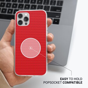 May include: Red phone case with a textured brick pattern, held in a hand. The case is compatible with PopSockets and is easy to hold. The phone case has a clear border and a camera cutout.