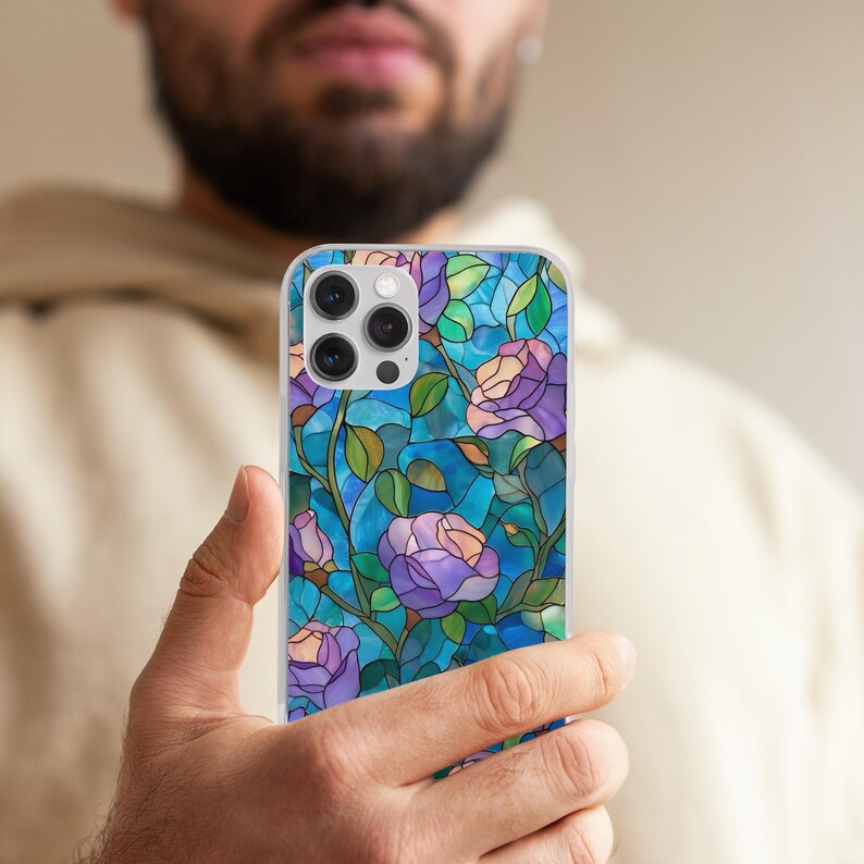 May include: A clear phone case featuring a stained-glass design of purple roses, green leaves, and blue background. The case has a glossy finish and is designed to fit a smartphone. The floral pattern is detailed and vibrant.