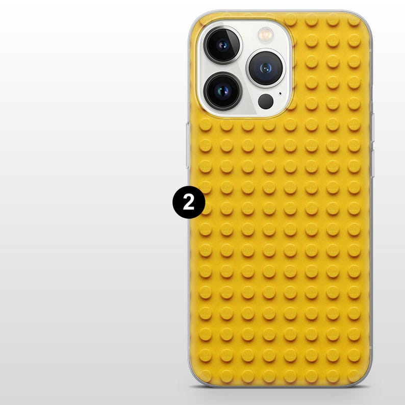 May include: Yellow phone case with a raised, textured design resembling toy building blocks. The case has a clear border and a black number 2 is visible on the side. The case is designed to fit a smartphone.