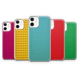 May include: A collection of colorful phone cases in pink, yellow, teal, red, and green. Each case has a textured surface with a pattern of small, raised circles, resembling toy building blocks. The cases have a clear border.