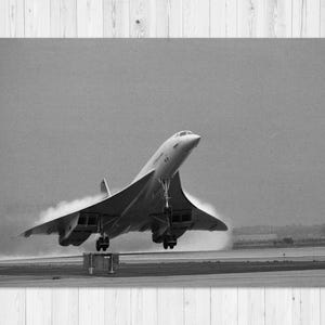 May include: Black and white photograph of a Concorde supersonic jet taking off. The aircraft is angled upwards, with its landing gear still extended. Vapor trails behind the plane. The image is set against a cloudy sky.