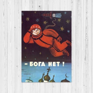 May include: A vintage-style poster featuring a cosmonaut in a bright orange suit with CCCP on the helmet, floating in a dark starry sky above church domes. A rocket ship is visible above, and the text reads - БОГА НЕТ ! in white letters.