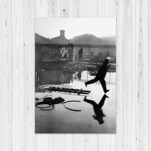 Puede incluir: Fotografía en blanco y negro de una persona corriendo sobre una superficie mojada, con su reflejo visible. El fondo incluye un edificio, una valla y un letrero. La imagen tiene un aspecto vintage y artístico.