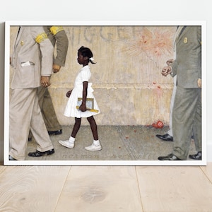 May include: Framed print of Norman Rockwell's painting, depicting a young Black girl in a white dress walking past figures in suits. The artwork is set against a textured wall with splatters of red. The print is displayed in a white frame.