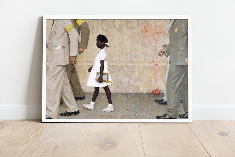 May include: Framed print of Norman Rockwell's painting, depicting a young Black girl in a white dress walking past figures in suits. The artwork is set against a textured wall with splatters of red. The print is displayed in a white frame.