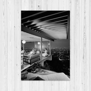 Puede incluir: Fotografía en blanco y negro de una casa moderna con grandes ventanales con vistas a una ciudad por la noche. Se ven personas dentro, y la arquitectura presenta un techo plano y un diseño minimalista.