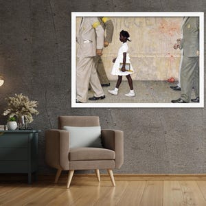May include: A framed print of Norman Rockwell's painting, "The Problem We All Live With." It depicts a young Black girl in a white dress walking past U.S. Marshals. The artwork is displayed on a gray wall above a brown armchair.