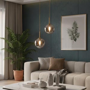 May include: A contemporary living room with a beige sofa, a marble coffee table, and two pendant lights with glass globe shades. The room is decorated with framed botanical prints and a large potted plant.