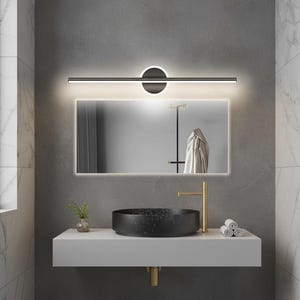 以下が含まれることがあります： 長方形の鏡、黒い円形の洗面台、金色の蛇口を備えたモダンなバスルームの洗面化粧台。洗面化粧台は白いカウンタートップと、鏡の上に黒とシルバーの照明器具を備えています。壁はグレーと白です。