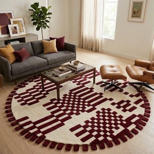 Può includere: Un grande tappeto circolare con una base color crema e un motivo geometrico di blocchi rettangolari bordeaux scuro. Il tappeto presenta un bordo strutturato composto da singoli ciuffi rettangolari bordeaux in rilievo.