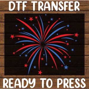 May include: DTF TRANSFER READY TO PRESS design. A graphic of a firework display in red and blue with star accents on a black background. The design is set against a wood grain background.