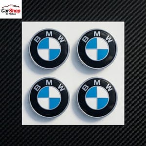 May include: A set of four circular BMW logo emblems arranged in a two-by-two grid on a white square backing. Each emblem features the iconic black outer ring with white BMW lettering, surrounding a central circle divided into blue and white quadrants.
