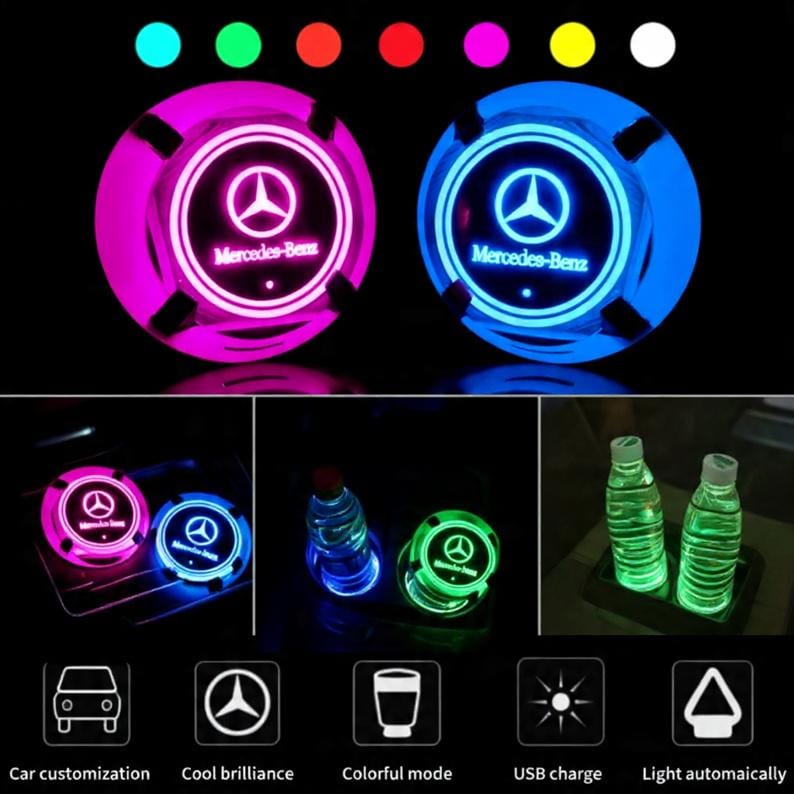 May include: Two circular LED car cup holder coasters featuring the Mercedes-Benz logo and text. The coasters emit various colors including pink, blue, and green. The image displays the coasters in use with water bottles and includes icons for USB charging, automatic lighting, and color modes.