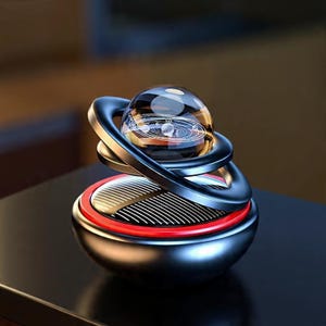 May include: A decorative object with a clear glass sphere at the centre, displaying a solar system design. The sphere is encircled by a dark blue, swirling ring. The base is metallic with a red accent.