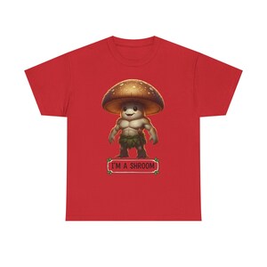 May include: Red t-shirt featuring a cartoon mushroom character with a muscular physique and a smiling face. The mushroom has a brown cap with white spots and is wearing a green leaf skirt. The text "I'M A SHROOM" is below the character.