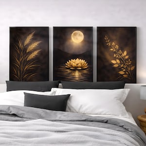 Op de afbeelding: Drie ingelijste wandkunstwerken. Het kunstwerk toont gouden botanische ontwerpen en een gouden lotusbloem met een volle maan boven het water. De achtergrond is donker en humeurig. De kunst wordt tentoongesteld boven een bed met wit en grijs beddengoed.