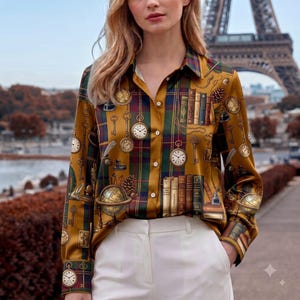 May include: A long-sleeved button-down shirt in a mustard yellow hue featuring a dark green and navy blue plaid pattern. The shirt is decorated with a print of vintage pocket watches, keys, stacks of books, globes, and pinecones.