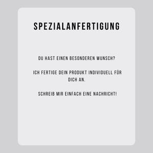 May include: A white rectangular card with rounded corners, featuring black text. The text reads "SPEZIALANFERTIGUNG" at the top, followed by several lines of German text. The card is set against a light gray background.