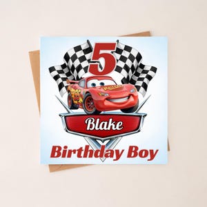 Peut inclure: Une carte d'anniversaire carrée illustrée d'une voiture de course rouge portant le numéro 95, deux drapeaux à damier noir et blanc et un grand chiffre 5 rouge. La carte affiche le prénom Blake et le texte Birthday Boy sur un emblème métallique.