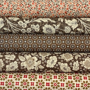Puede incluir: Una pila de rollos de tela con varios estampados florales. El rollo superior presenta pequeñas flores rojas y marrones sobre un fondo crema. Otros rollos muestran diseños florales marrones y crema, y un estampado de lunares marrones y blancos.
