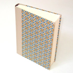 Puede incluir: Un libro de tapa dura con una cubierta beige y una columna vertebral con un patr&oacute;n azul y amarillo.