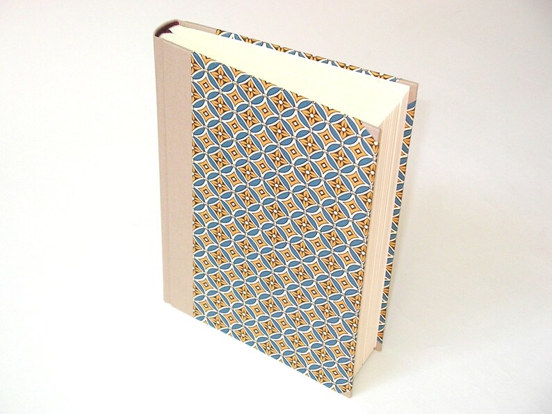 Puede incluir: Un libro de tapa dura con una cubierta beige y una columna vertebral con un patr&oacute;n azul y amarillo.