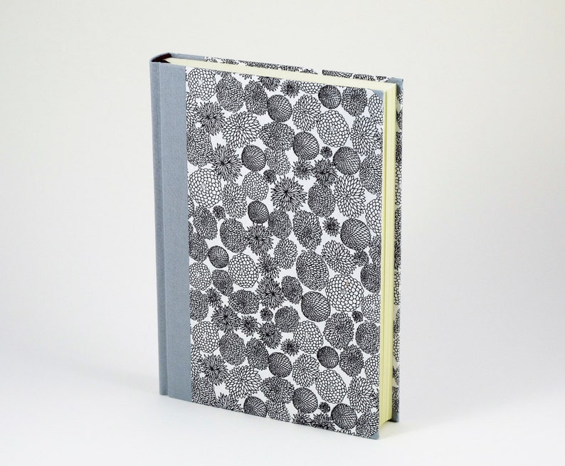 May include: A gray hardcover journal with a white cover featuring a black and white floral pattern.