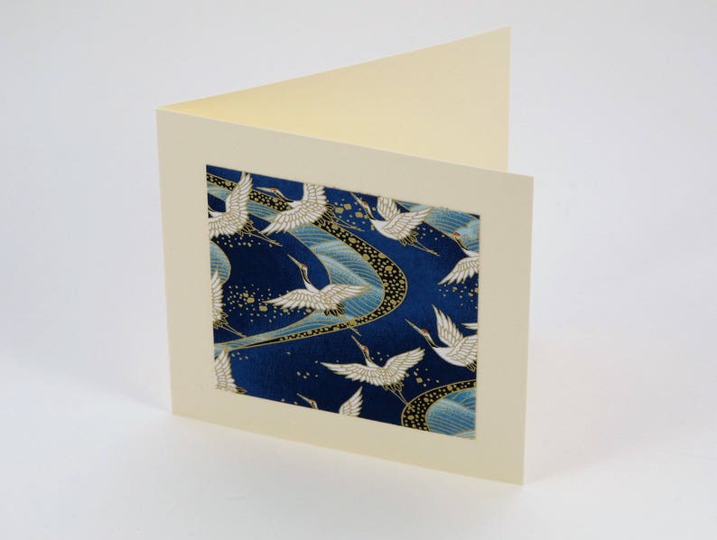 May include: A blank card with a cream-colored border and a blue and gold patterned insert featuring white cranes flying in a swirling pattern.