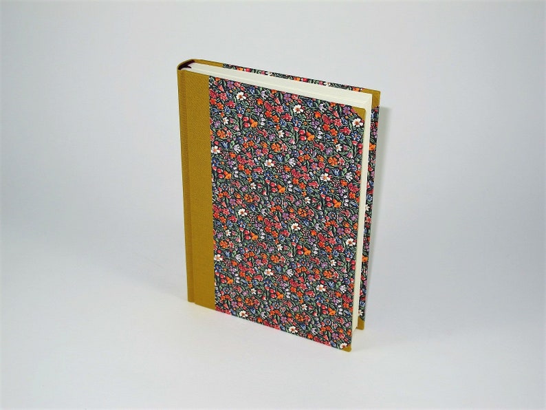 May include: A hardcover book with a floral pattern cover and a mustard-colored spine. The cover features a dark background with a repeating pattern of small red, orange, and white flowers. The book is standing upright.