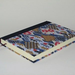 May include: A blue and gold patterned journal with a red bookmark. The cover is made of fabric with a Japanese-inspired design.
