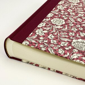 May include: A hardback book featuring a burgundy spine and a floral pattern in burgundy and white. The pages are cream-coloured, and the binding is gold.