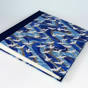 May include: A blue and white photo album with a Japanese crane pattern. The cover is made of fabric and has a navy blue border.