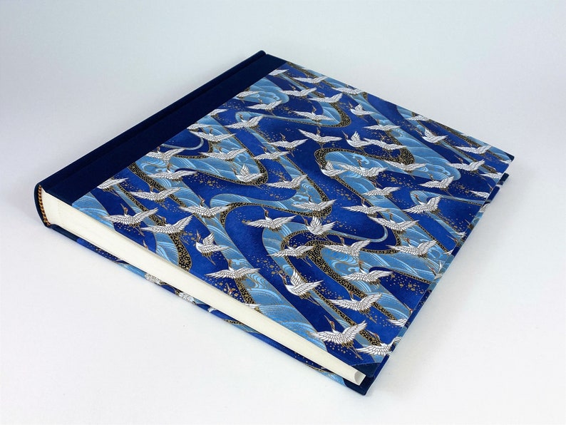 May include: A blue and white photo album with a Japanese crane pattern. The cover is made of fabric and has a navy blue border.