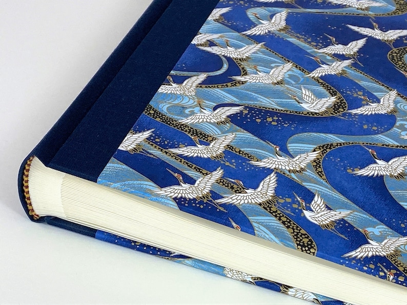 May include: A blue photo album with a white crane pattern on the cover. The album has a navy blue spine and gold accents.