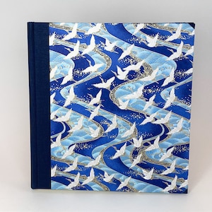 May include: A blue and white fabric-covered journal with a pattern of white cranes flying over blue waves. The journal has a dark blue spine.