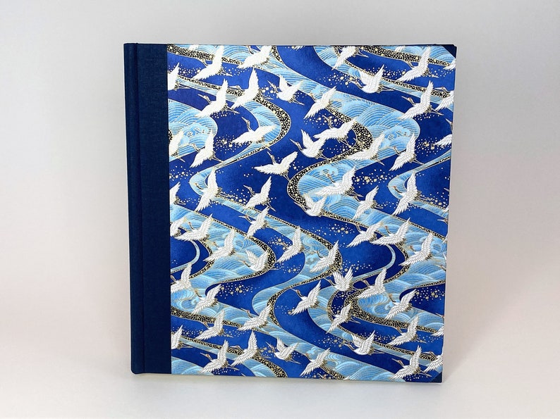 May include: A blue and white fabric-covered journal with a pattern of white cranes flying over blue waves. The journal has a dark blue spine.