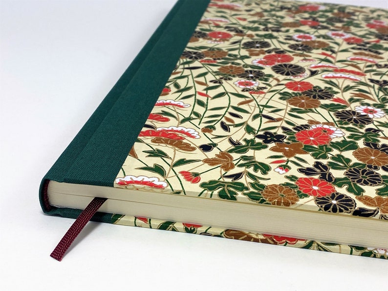 Op de afbeelding: Een groen en cr&egrave;mekleurig hardcover-journaal met een bloemenpatroon en een bordeauxrode lint-bladwijzer. Het journaal heeft een groene rug en een cr&egrave;mekleurige omslag met een bloemenpatroon.