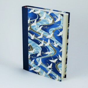 May include: A blue and white journal with a pattern of white cranes flying over blue waves. The journal has a dark blue spine and a white cover.