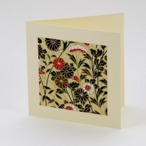May include: A blank card with a cream coloured background and a square window showing a floral pattern in black, white, red, and gold.