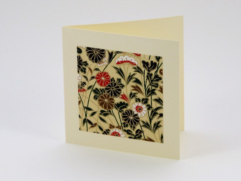 May include: A blank card with a cream coloured background and a square window showing a floral pattern in black, white, red, and gold.