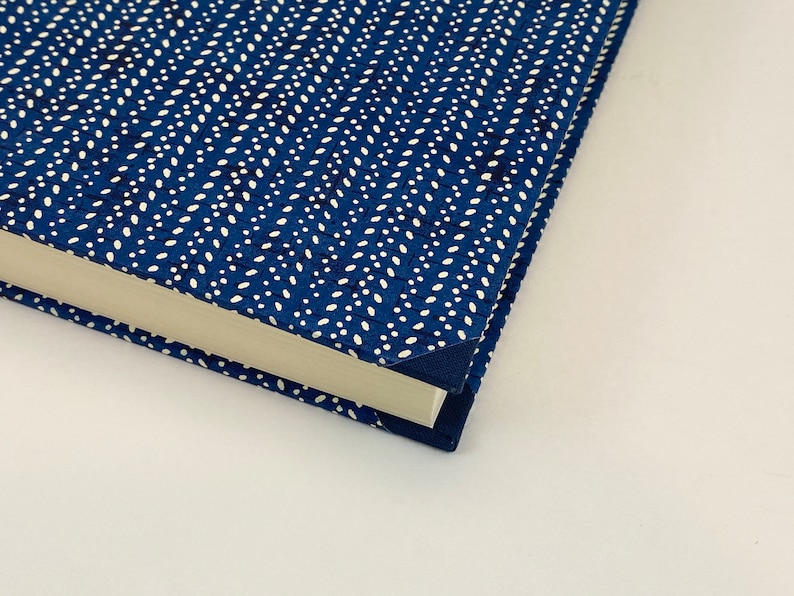 Pode incluir: Close-up do canto de um livro azul com um padr&atilde;o de bolinhas brancas. O livro est&aacute; fechado e a lombada &eacute; vis&iacute;vel.