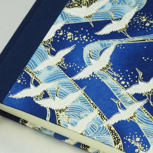 May include: A blue fabric-covered journal with a gold and white crane pattern. The journal has a dark blue spine and a ribbon bookmark.