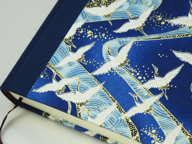 May include: A blue fabric-covered journal with a gold and white crane pattern. The journal has a dark blue spine and a ribbon bookmark.