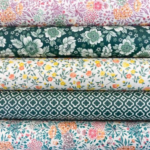 Könnte beinhalten: Stapel von Stoffrollen mit verschiedenen floralen und geometrischen Mustern. Die Stoffe zeigen Farben wie Rosa, Orange, Grün und Weiß. Die Designs umfassen große Blumen, kleine Blüten und ein sich wiederholendes Kleeblattmuster.