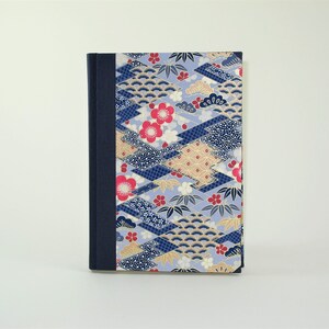 May include: A blue and gold patterned notebook with a dark blue spine. The cover features a repeating pattern of geometric shapes, flowers, and leaves.