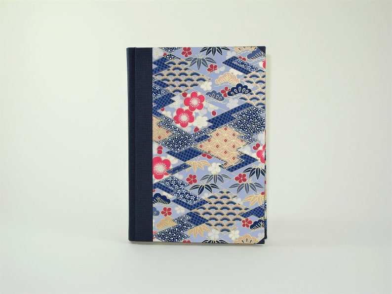 May include: A blue and gold patterned notebook with a dark blue spine. The cover features a repeating pattern of geometric shapes, flowers, and leaves.