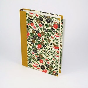 May include: A hardcover journal with a floral design on the cover. The cover features a white background with red, black, and green flowers and leaves. The spine is a solid gold colour.