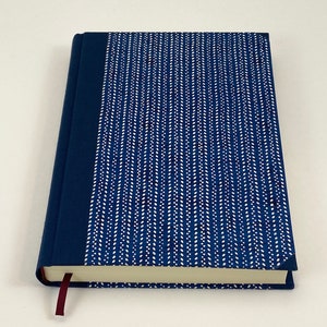 Pode incluir: Um di&aacute;rio de capa dura azul com um design estampado branco e um marcador de fita cor vinho.