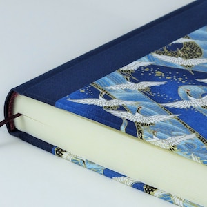 May include: A blue hardcover journal with a gold and white crane pattern on the cover. The journal has a dark blue spine and a burgundy ribbon bookmark.